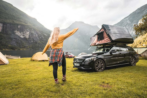  Eine Frau läuft über einen Campingplatz am See zu ihrem Mercedes mit Dachzelt