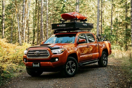 X-Cover Dachzelt mit Kanu auf einem orangenen Pickup-Truck, der im Wald parkt