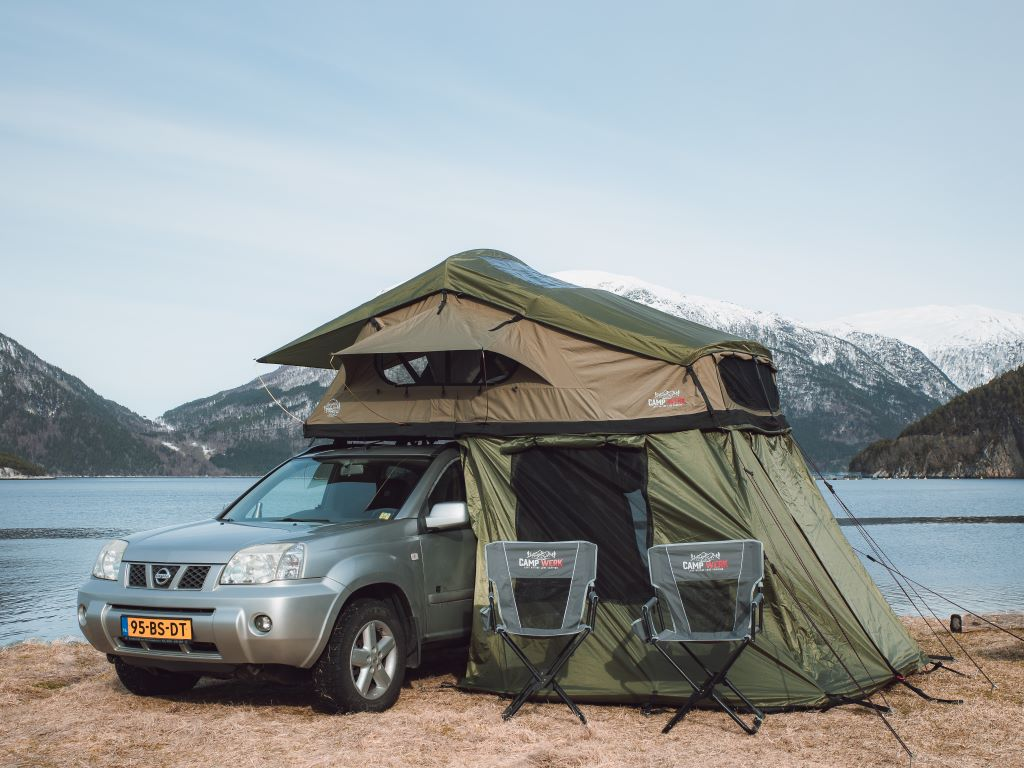 Groene CAMPWERK daktent op een auto met kampeerstoelen en luifel aan een bergmeer