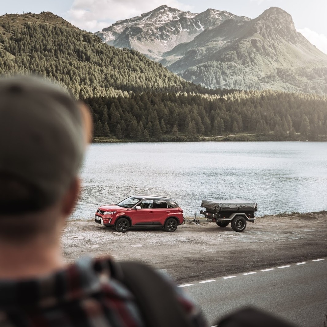 Person blick auf ein Auto mit abgekuppeltem Zeltanhänger am See