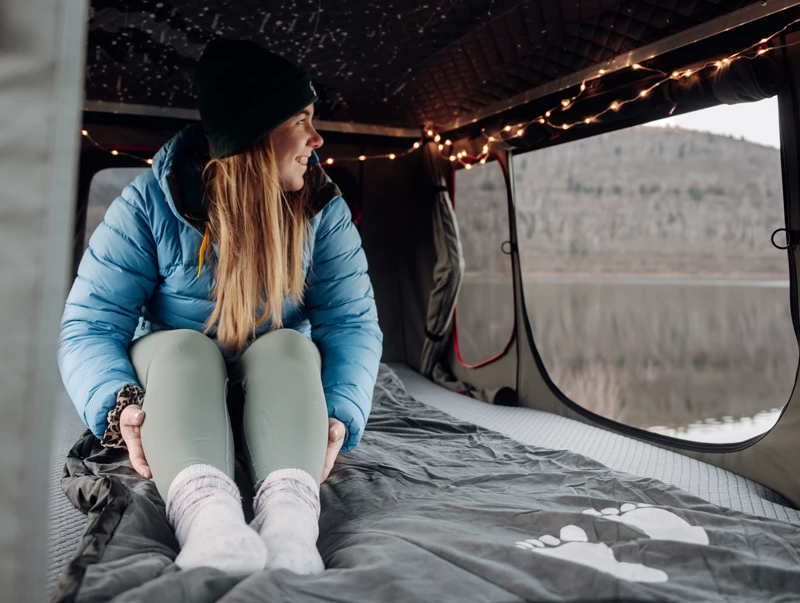 Camperin sitzt auf einer Heizdecke in ihrem Dachzelt im Winter